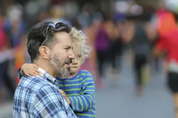 Pappa med ett barn på armen i förgrunden, människor i bakgrunden