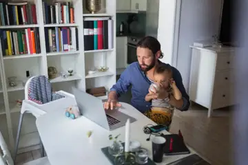 Pappa sitter framför datorn med sitt barn i knät